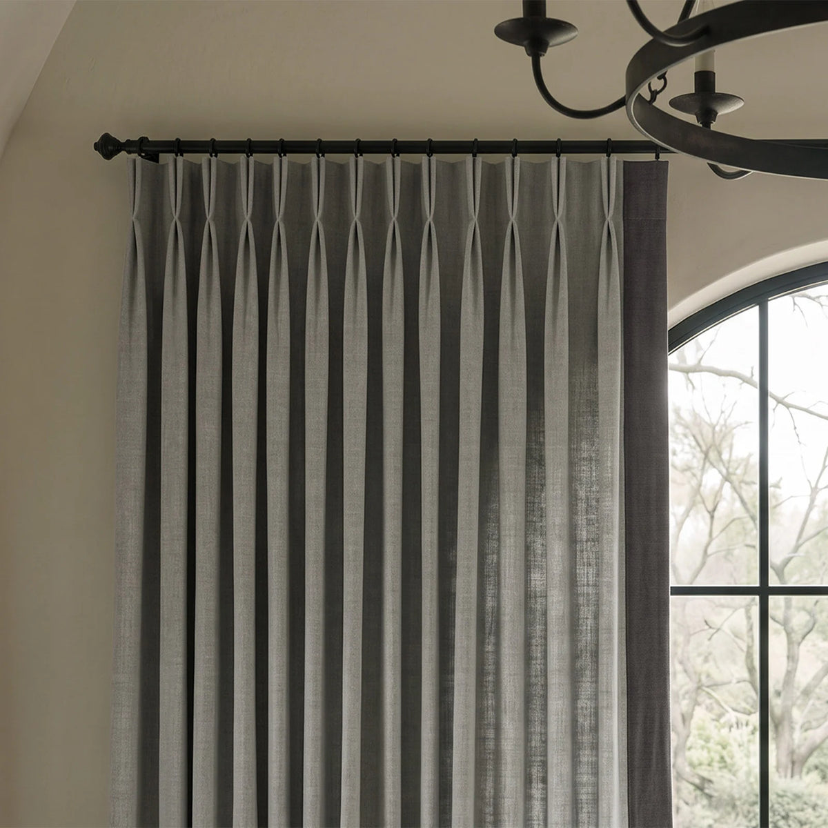 Close-up of two-tone pinch pleat curtains showing the contrasting leading-edge border and fabric texture, shown in a closer material view.