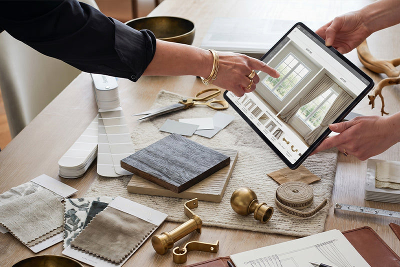 Designer and client reviewing window plans and fabric samples on a table.