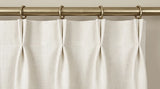 Ivory French pleat curtain header hanging from brass rings and a brass rod.