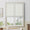 Ivory woven flat Roman shade partially lowered over a white framed window in a bright living room