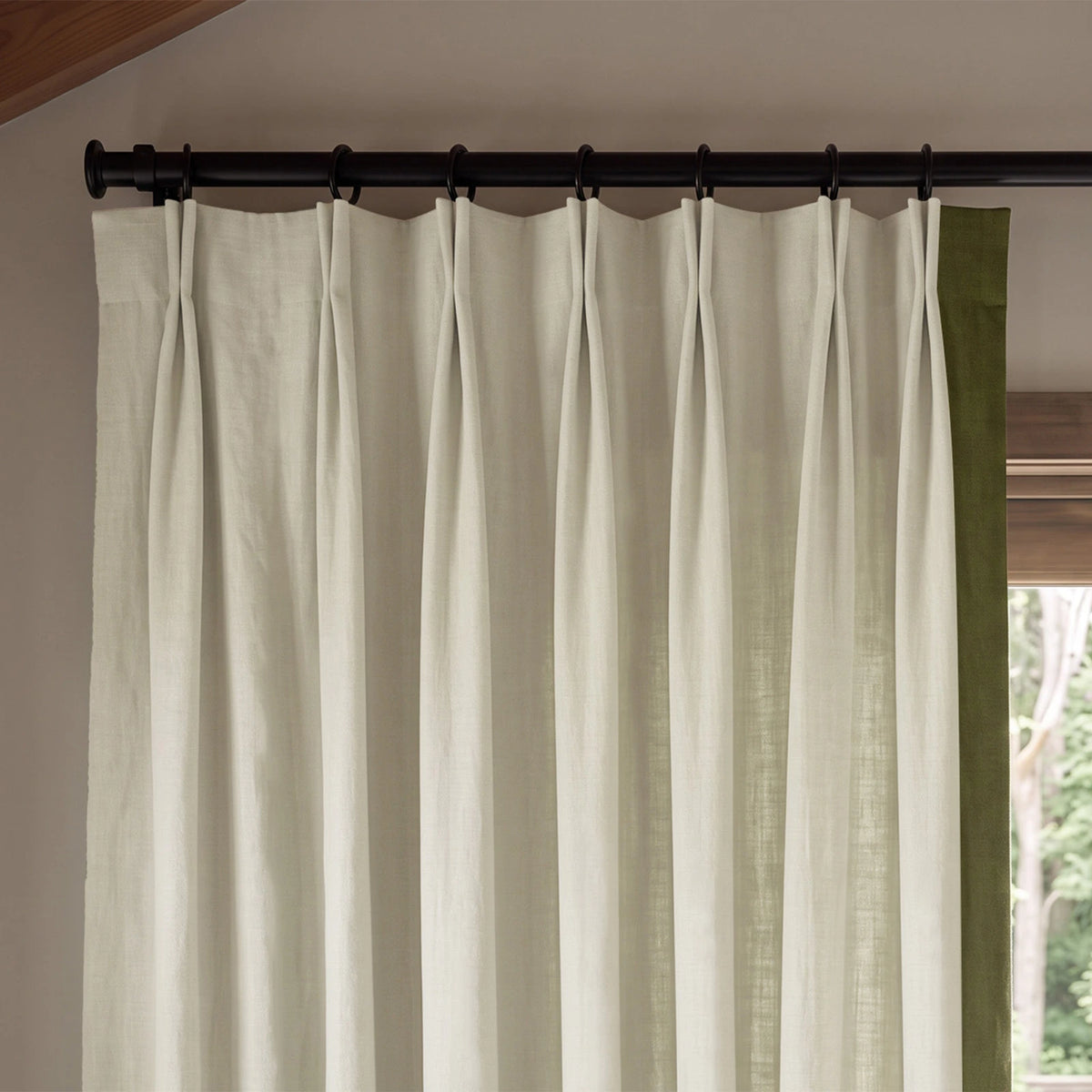 Close-up of two-tone pinch pleat curtains showing the contrasting leading-edge border and fabric texture, shown in a full-window view.